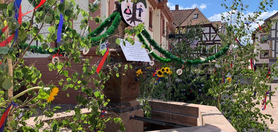 Brunnen geschmückt mit Bändern und Birkenzweigen sowie einem Brunnenspruch