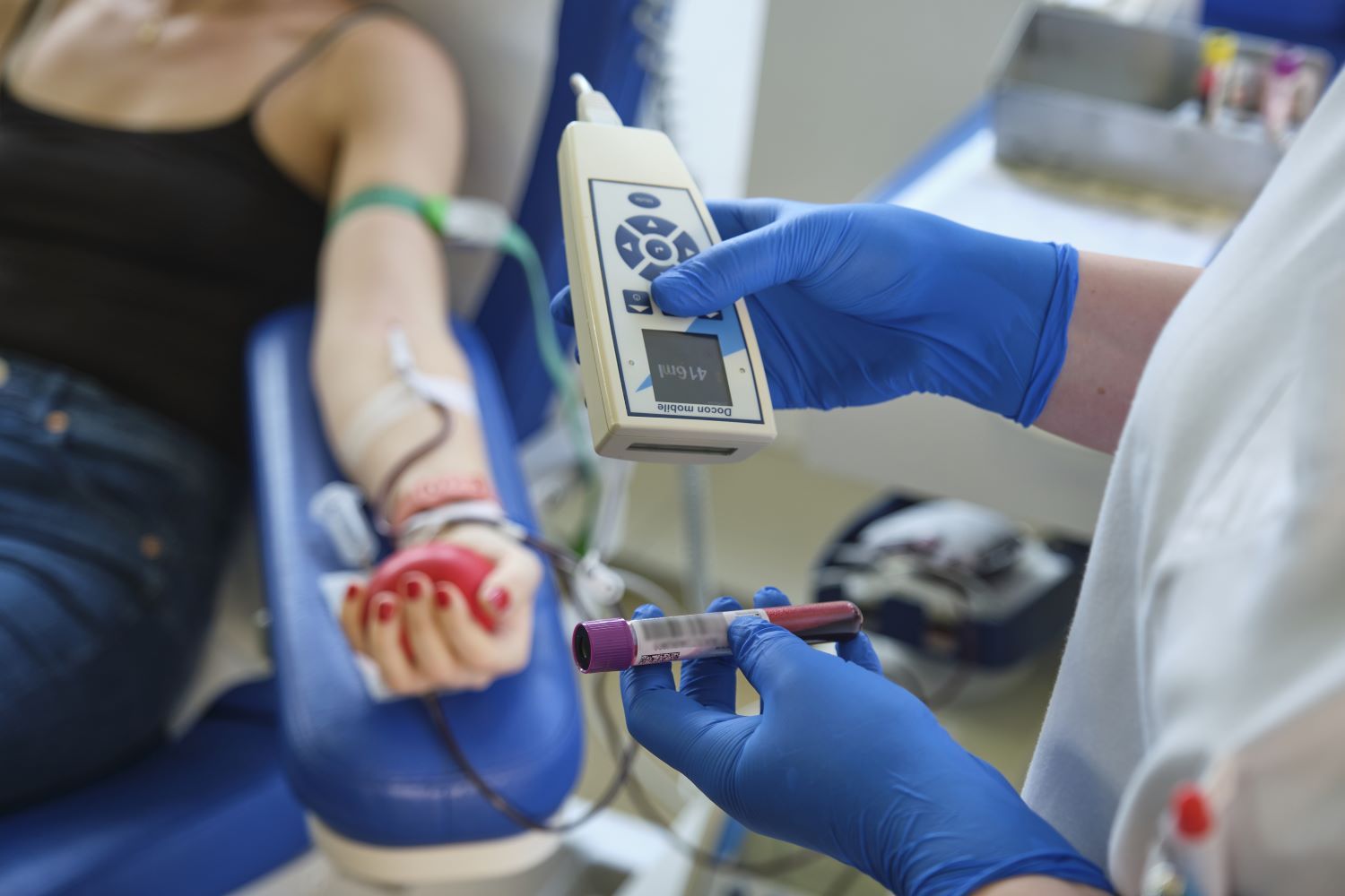 Arm einer Frau, die grade Blutspendet mit DRK-Helfer, der Blutprobe in Händen hält