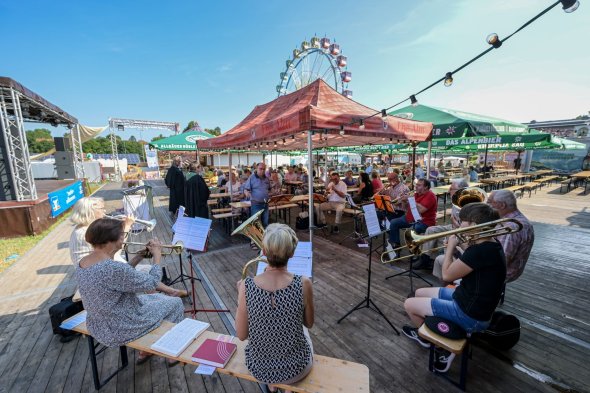 Posaunenchor vor Zuhörenden, die auf Biertischgarnituren vor einem Riesenrad sitzen