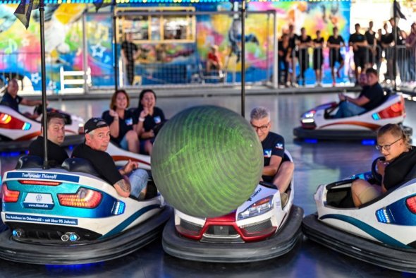 Menschen im Autoscooter fahren gegen einen Ball, der durch die Luft fliegt.