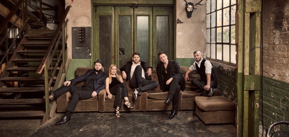 Fünf Musiker auf Sofa vor Wand mit Jagdtrophäen