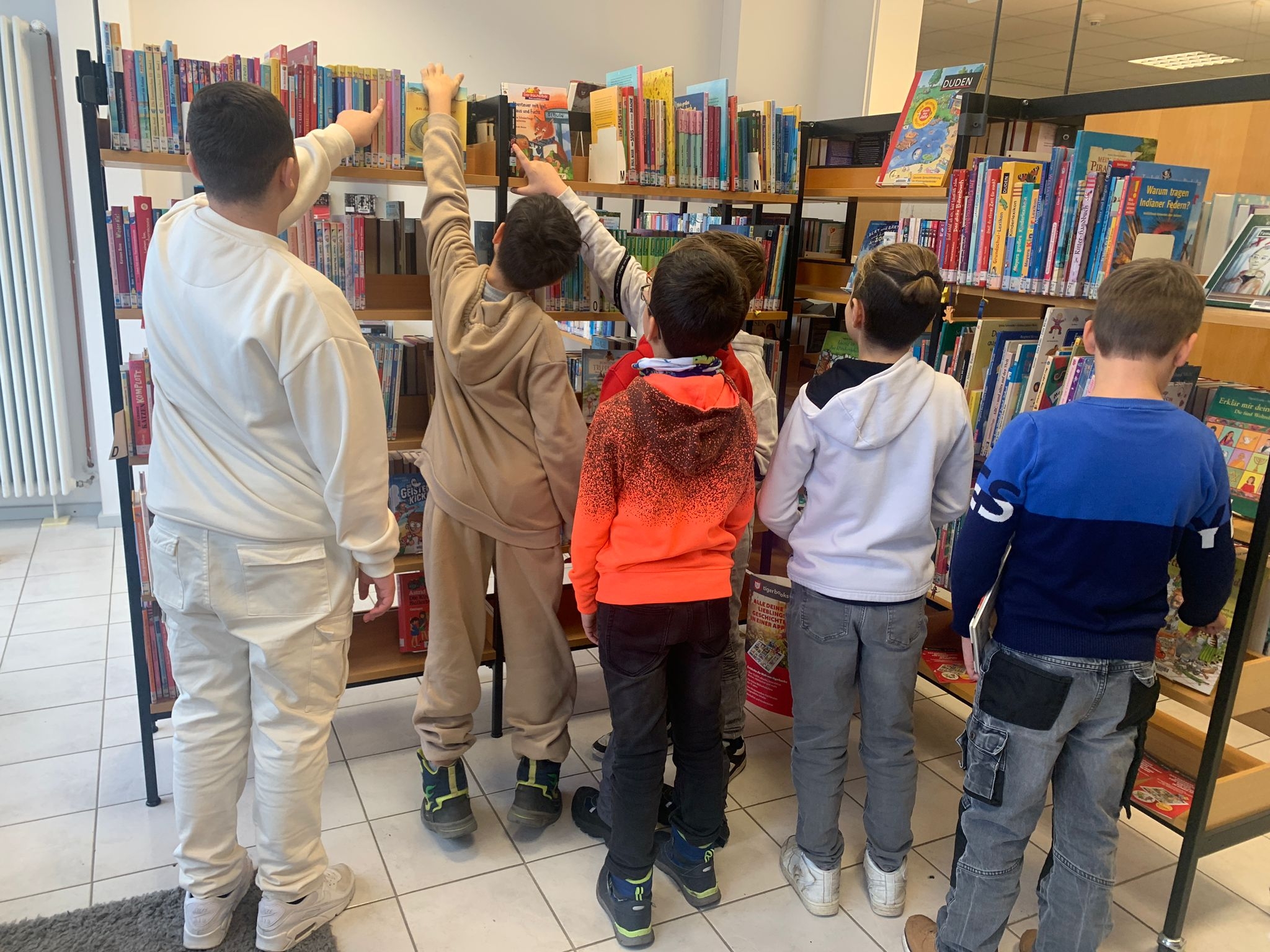 Schüler stehen vor Bücherregal und deuten auf Bücher