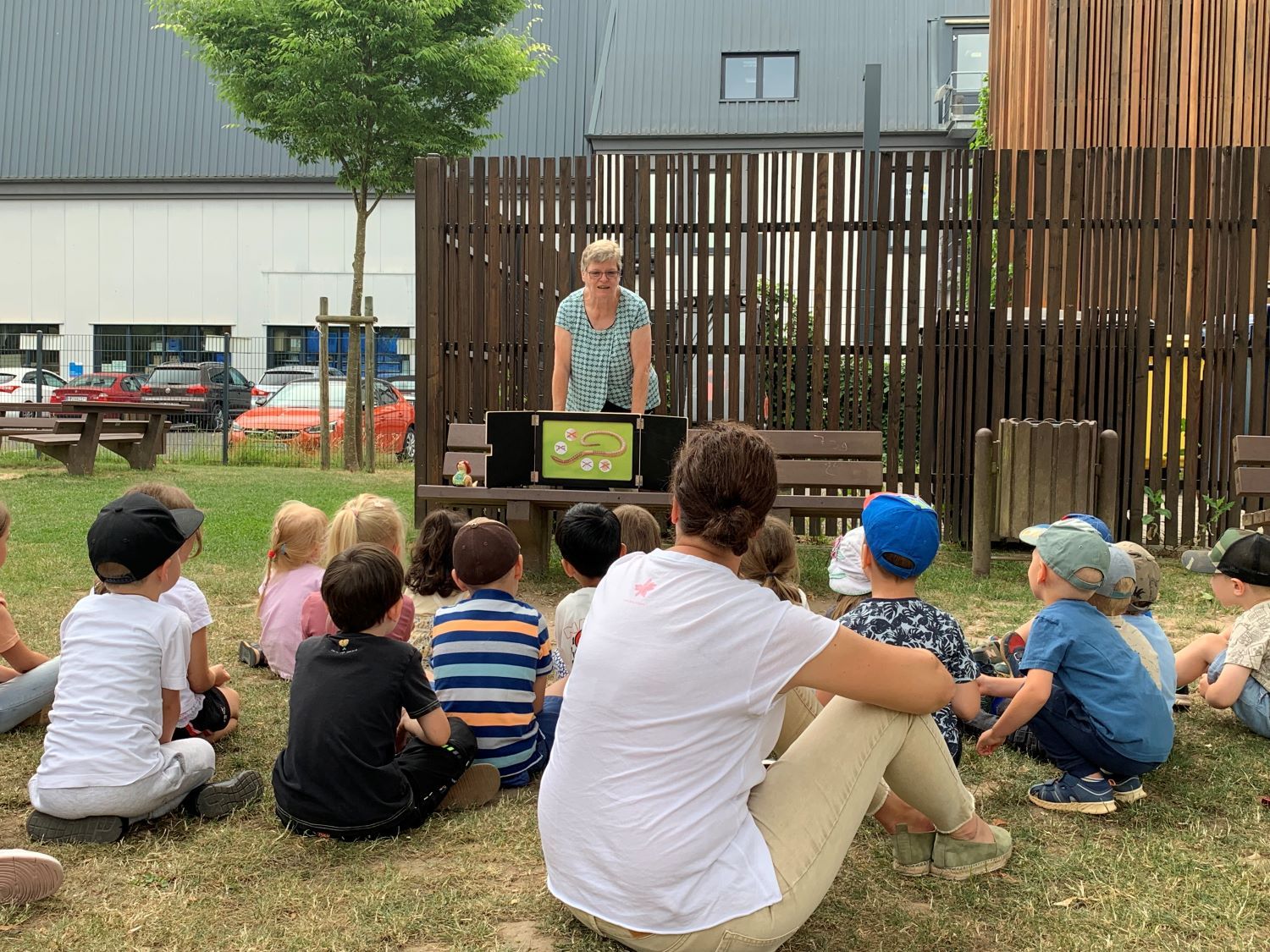 Kita-Kinder sitzen auf Wiese und hören Geschichte zu