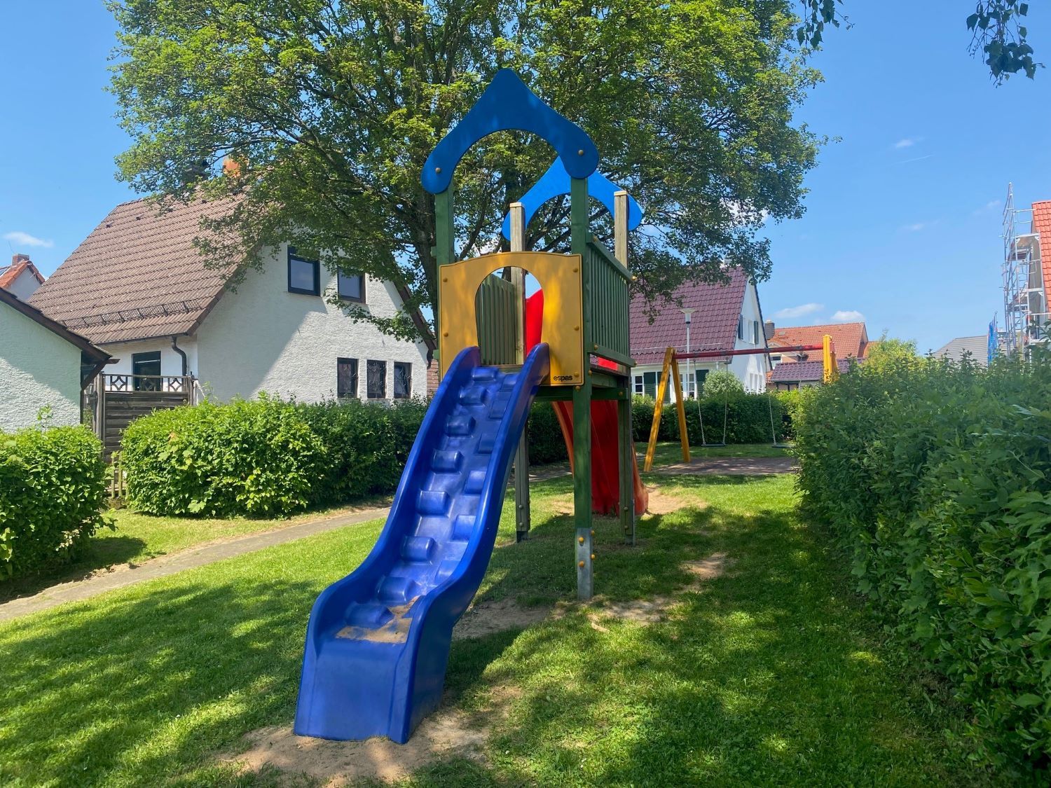 Rutschturm auf Spielplatz mit Haus im Hintergrund