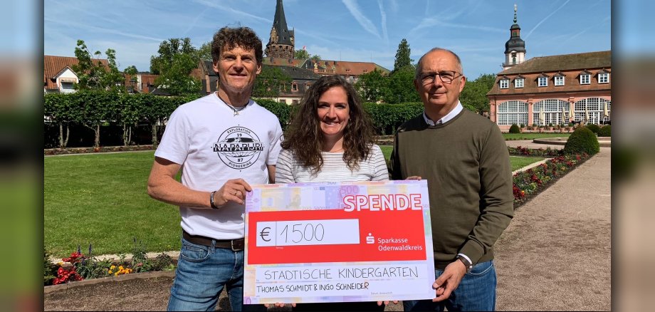 Zwei Männer und eine Frau mit übergroßem Scheck inr Gartenanlage