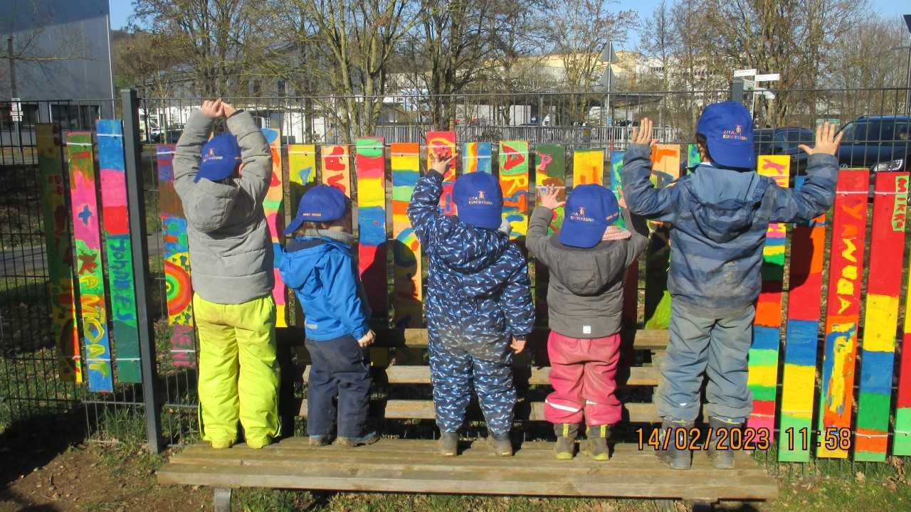 Kita-Kinder stehen mit dem Rücken zur Kamera und tragen blaue Kappen