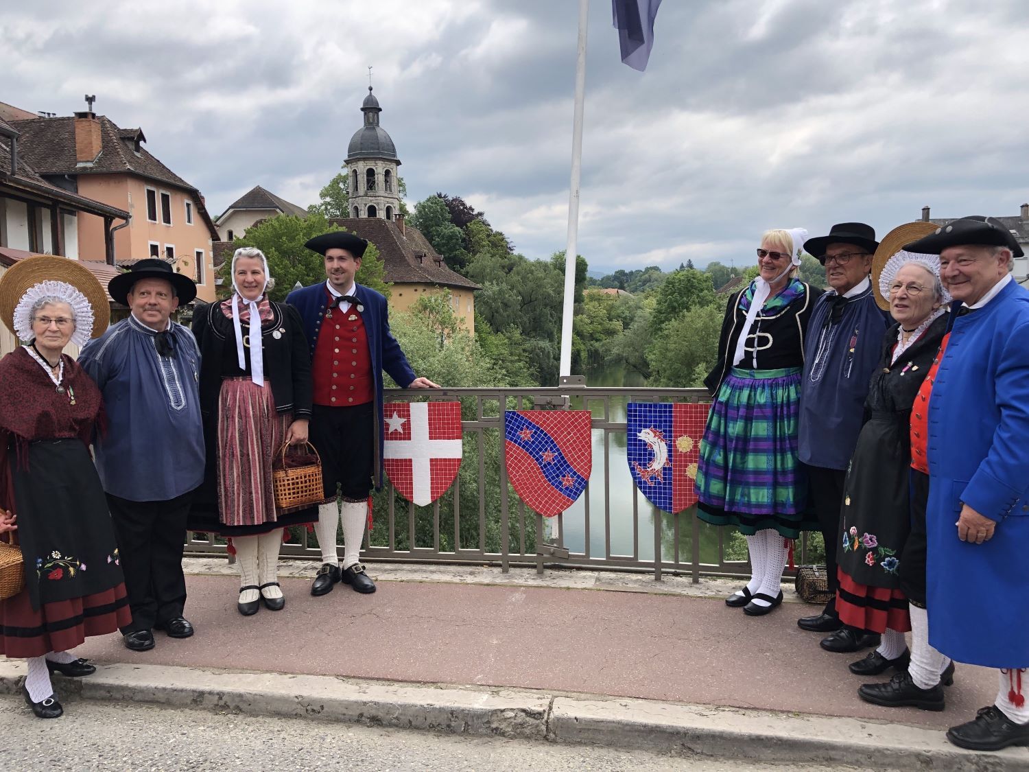 Mitglieder zweier Trachtengruppen in Tracht auf Brücke mit Wappen