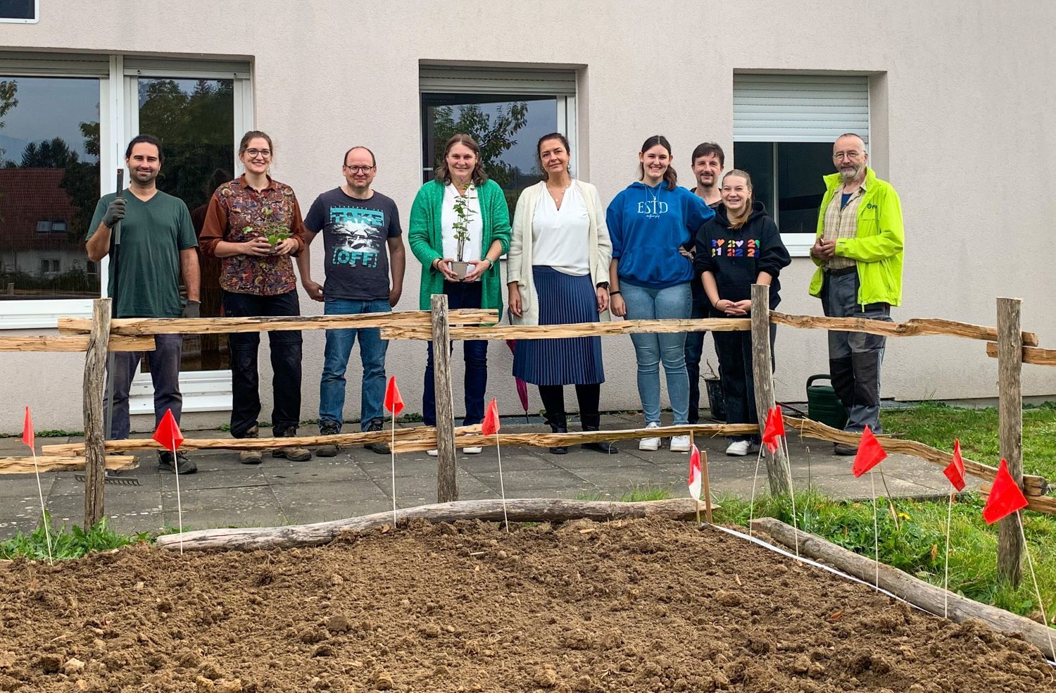 Männer und Frauen mit Spaten und Pflanzen vor Pflanzbeet