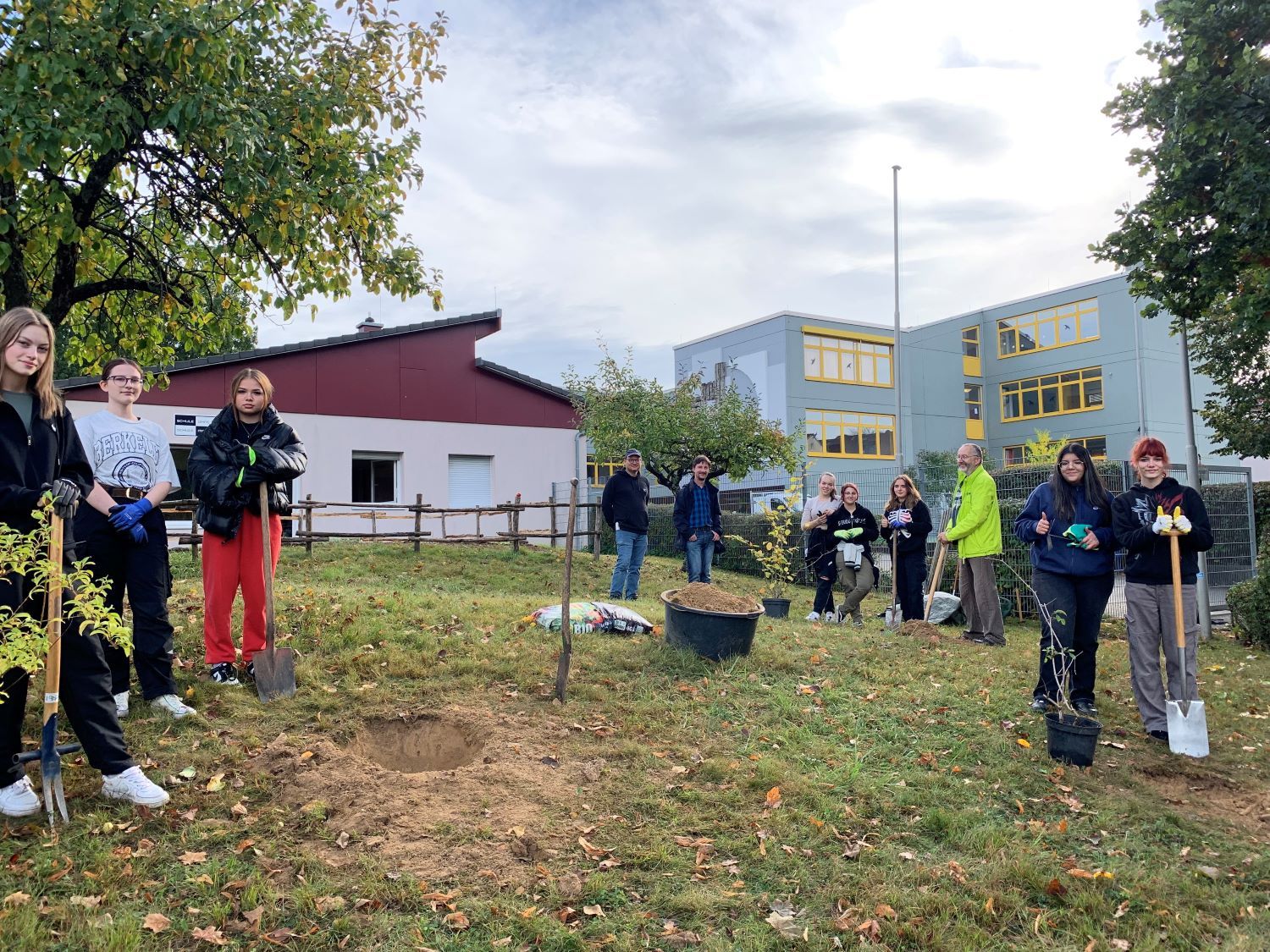 Schülerinnen und Schüler mit Spaten und Pflanzen in einem Garten