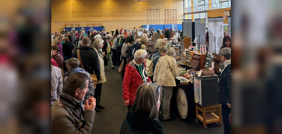 Interessierte in den Händlerhallen des Klöppelspitzenkongresses Viele Personen, die sich Waren (Spitzendecken) von Händlern in einer Sporthalle ansehen.