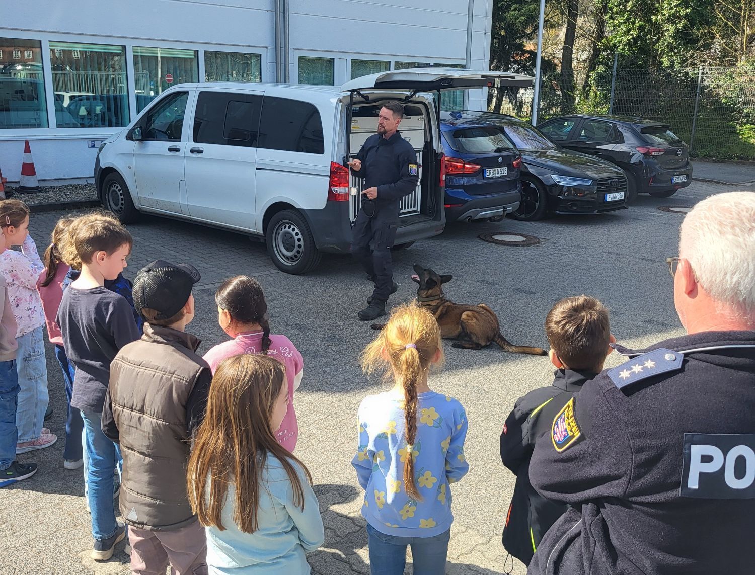 Kinder, die einem Polizisten zusehen, der etwas anhand eines Polizeihunds erklärt