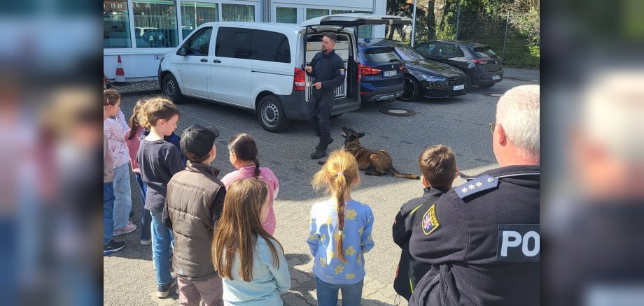 Kinder, die einem Polizisten zusehen, der etwas anhand eines Polizeihunds erklärt