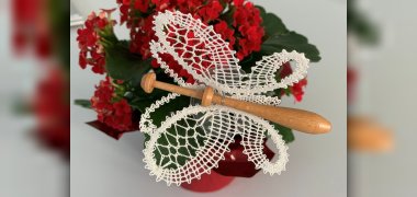 Schmetterling, der aus Klöppelspitze gefertigt wurde und auf roten Blumen angebracht ist.