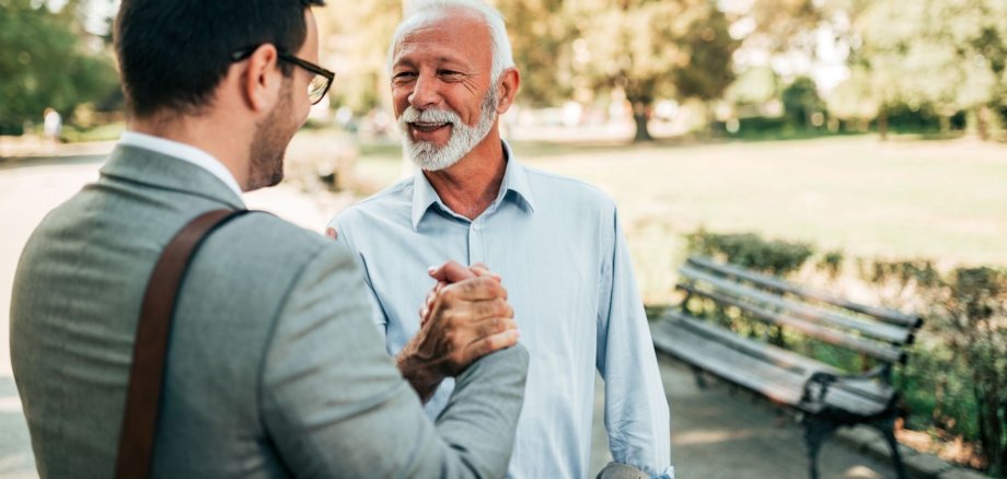 Mentor hilft jungem Menschen Ein jüngerer Mann und ein älterer Mann begrüßen sich per Handschlag.