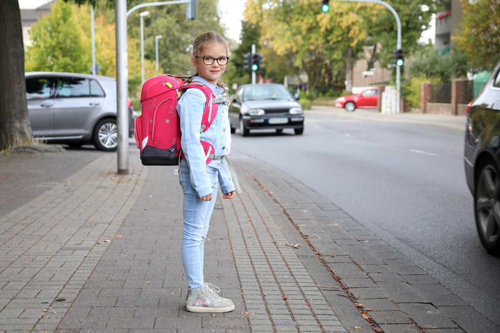 Mädchen mit Schultornister möchte die Strasse überqueren.