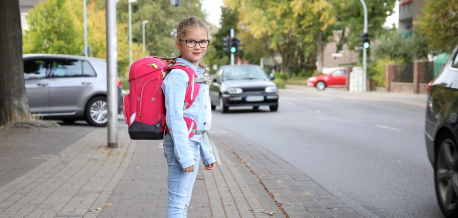 Mädchen mit Schultornister möchte die Strasse überqueren.