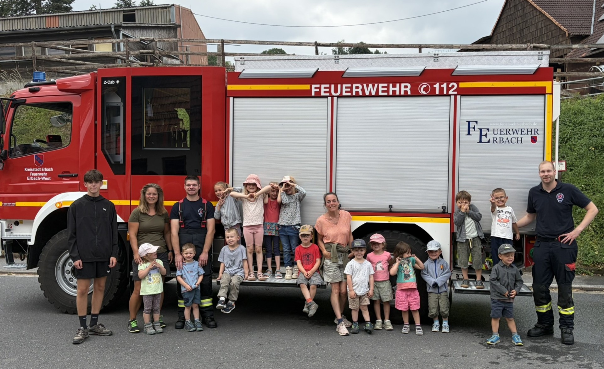Kita-Kinder posieren gemeinsam mit ihren Erziehern und zwei Feuerwehrmännern vor einem Feuerwehrauto