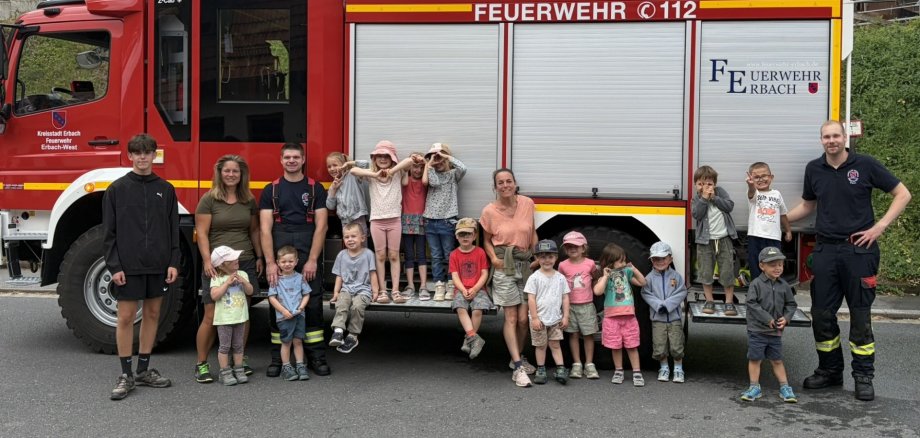 Kita-Kinder posieren gemeinsam mit ihren Erziehern und zwei Feuerwehrmännern vor einem Feuerwehrauto