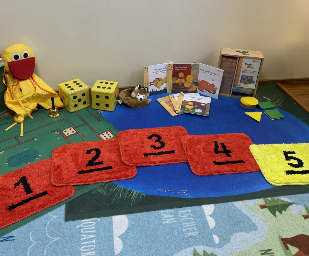 Verschiedene Lernspielzeuge für Kinder, darunter Decken mit Zahlen, eine Entenpuppe und Würfel.