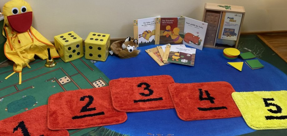 Verschiedene Lernspielzeuge für Kinder, darunter Decken mit Zahlen, eine Entenpuppe und Würfel.