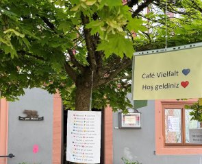 Willkommen im Café Vielfalt Willkommensschilder, die an einem Baum hängen