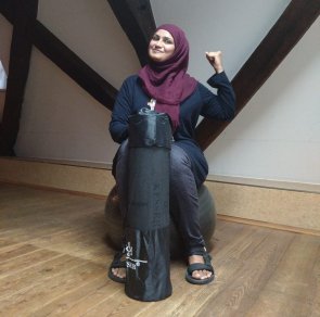 Yoga-Stunde für Frauen mit Kiran Fatima Frau mit Hijab hält eine Yoga-Matte in der Hand und hat den Arm gebeugt als Zeichen von Stärke