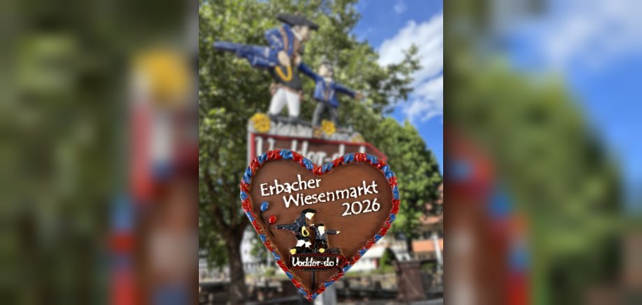 Wiesenmarktsherz 2026 Ein Herz-Anstecker aus Ton vor einem nostalgischen Toilettenschild mit der Aufschrift "Vadder Do"