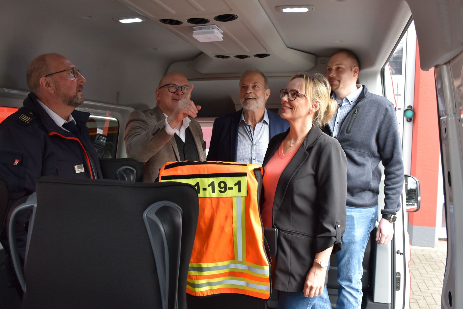 Menschen stehen in einem Feuerwehrfahrzeug und zeigen auf einen Rauchwarnmelder