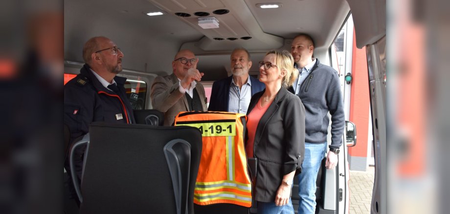 Menschen stehen in einem Feuerwehrfahrzeug und zeigen auf einen Rauchwarnmelder