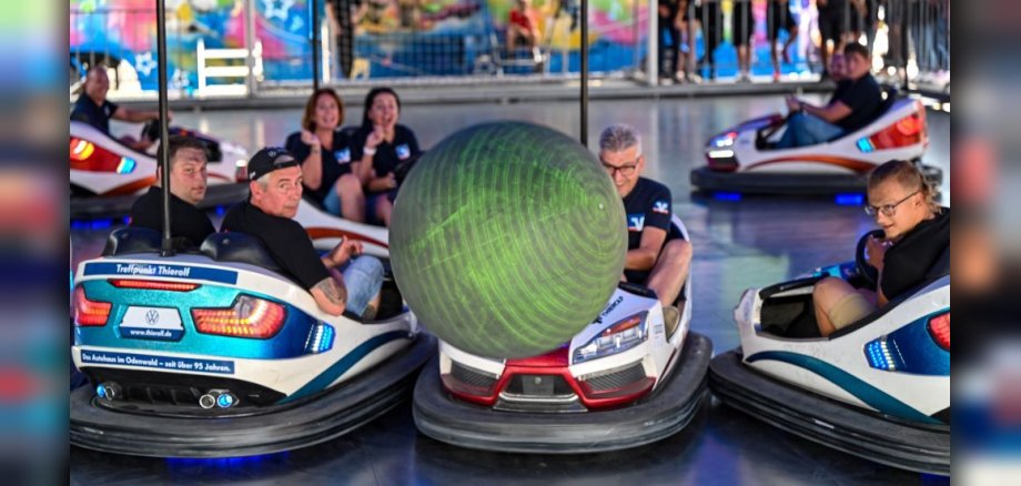 Menschen im Autoscooter fahren gegen einen Ball, der durch die Luft fliegt.