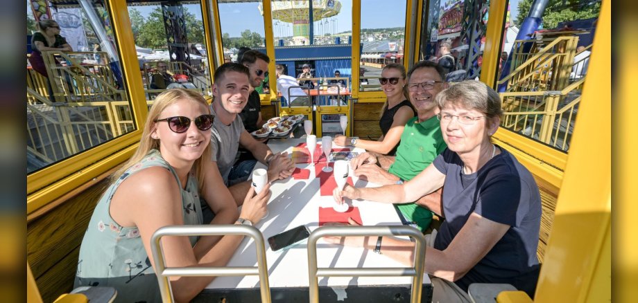 Sechs Personen sitzen in einer Riesenad-Gondel und haben Frühstück vor sich stehen.