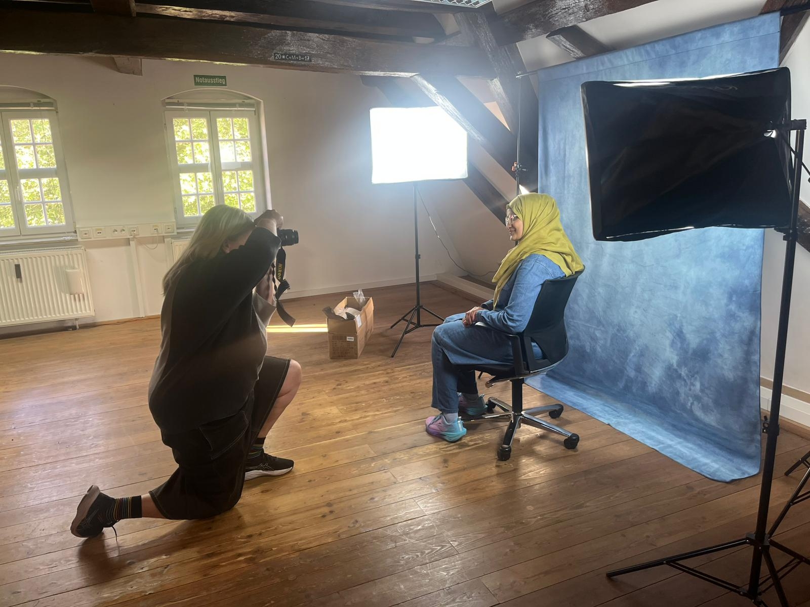 Eine Person fotografiert eine andere Person, die vor einer Fotoleinwand sitzt