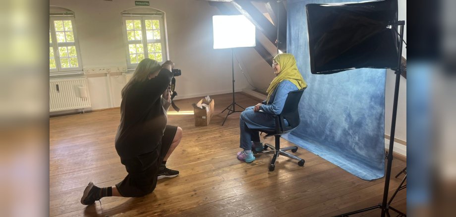 Eine Person fotografiert eine andere Person, die vor einer Fotoleinwand sitzt