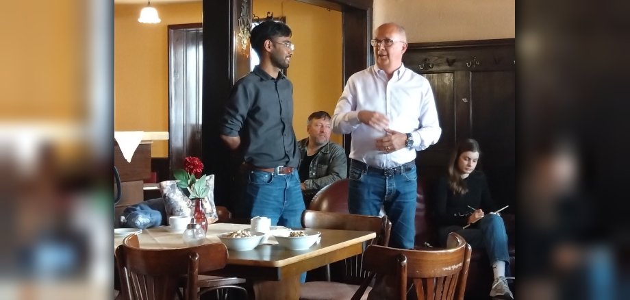 Eröffnungsfeier des Café Vielfalt Zwei Männer halten eine Rede in den Räumlichkeiten eines Cafés