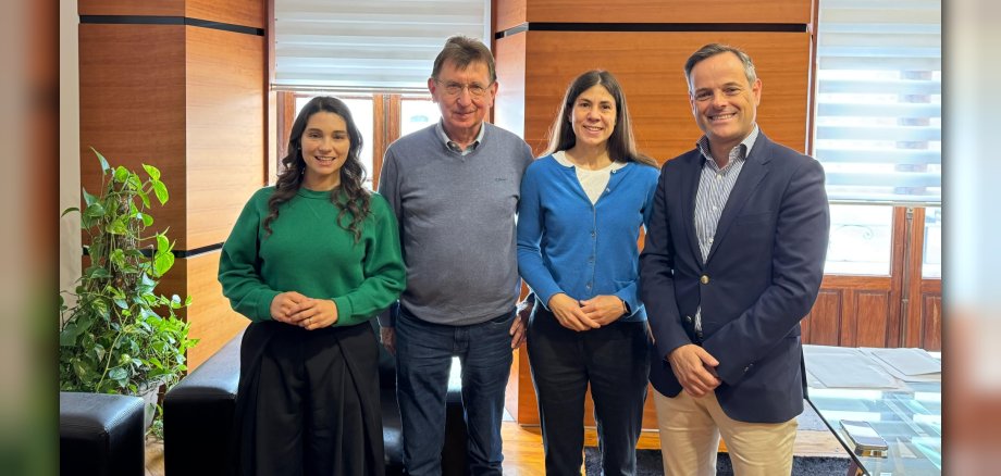 Claudia und Erich Petersik (Mitte) übergeben symbolisch die Spende von 1.800 Euro, die im Rahmen einer Go-Fund-Me-Initiative zur Aufforstung des Stadtwalds gesammelt wurden, an Ansiãos Bürgermeister Jorge Humberto Fernando Cancelinha (rechts) und Stadträtin Maria Goreti da Silva Correia (links). Vier Personen, zwei Frauen und zwei Männer, stehen in einem Büro und lächeln in die Kamera.