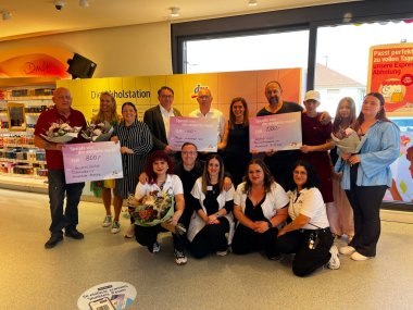 Gruppenbild mit übergroßen Spenden-Schecks und Blumensträußen