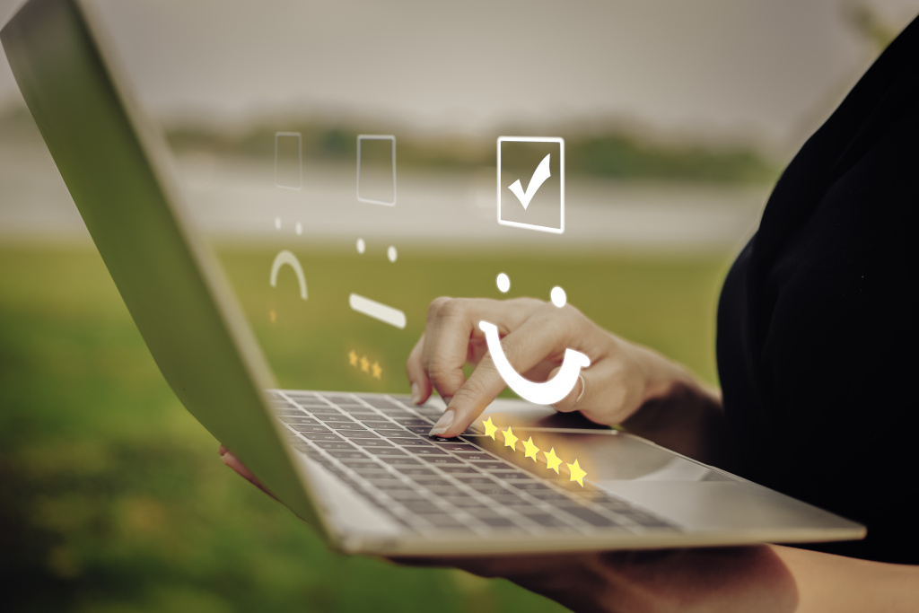 Finger tippen auf einem Laptop herum. Darüber ist ein Smiley mit Bewertungssternen zu sehen.