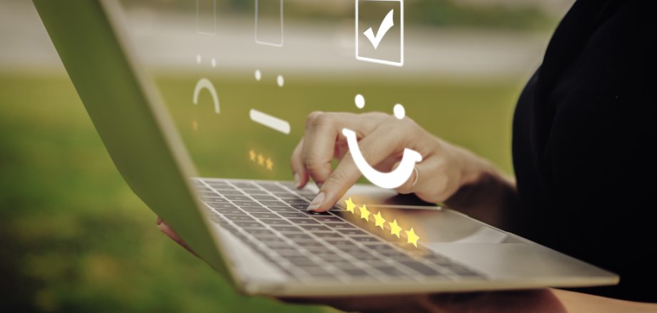 Online-Umfrage Finger tippen auf einem Laptop herum. Darüber ist ein Smiley mit Bewertungssternen zu sehen.