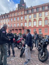 1. Stadtrat Dominik Weyrauch im Gespräch beim Fellows Ride Odenwald. Menschen stehen vor geparkten Motorräder auf einem historischen Marktplatz und unterhalten sich.