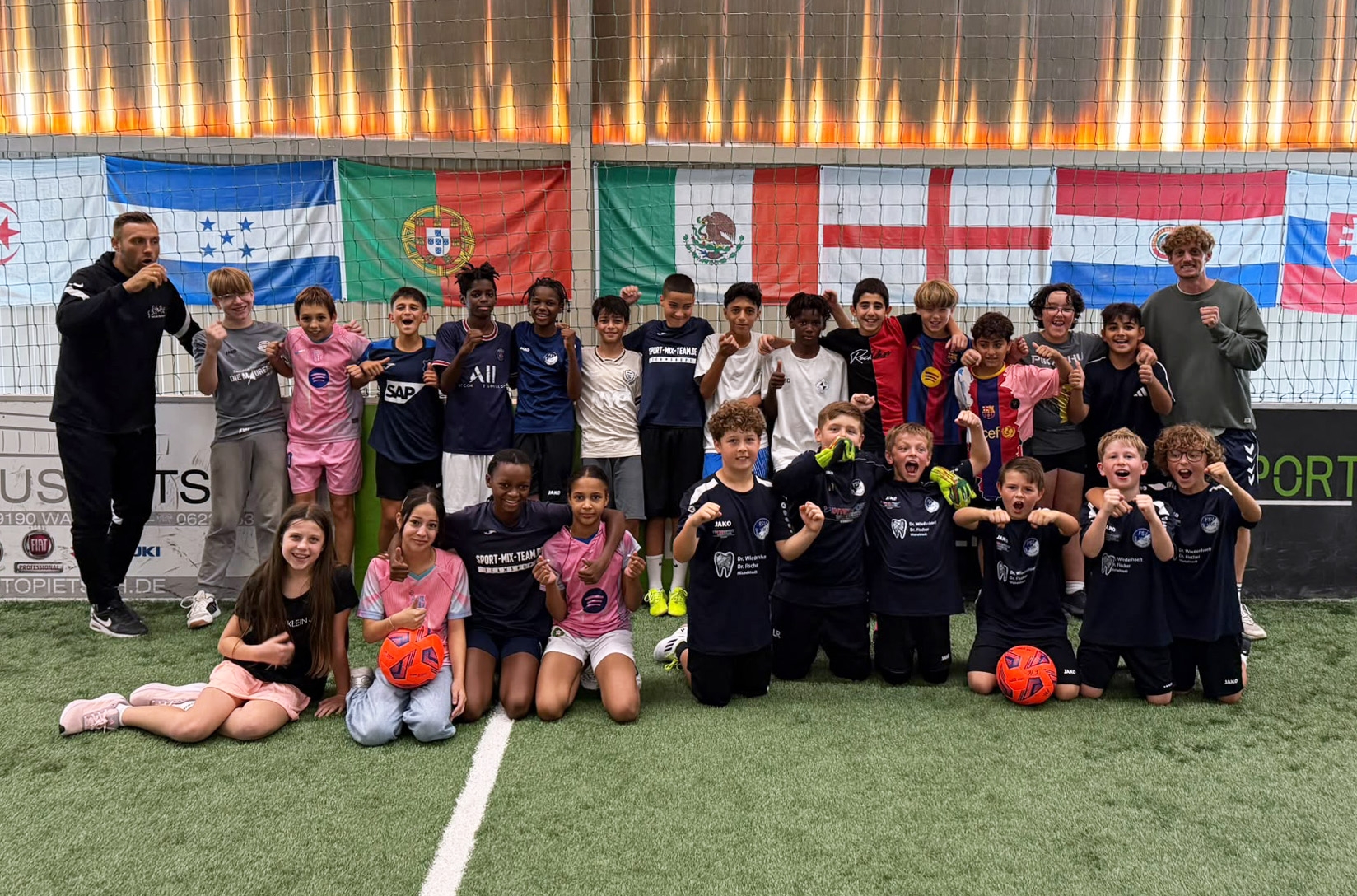 Gruppenfoto von Kindern mit zwei Betreuern in einer Indoor-Fußballhalle
