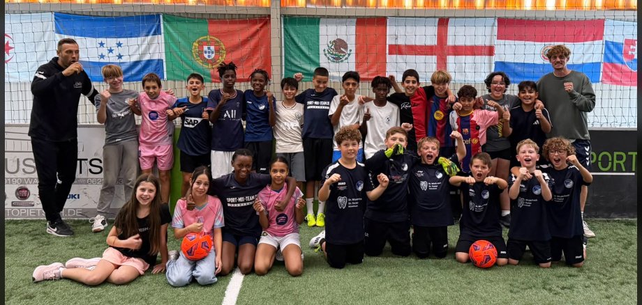 Gruppenfoto von Kindern mit zwei Betreuern in einer Indoor-Fußballhalle
