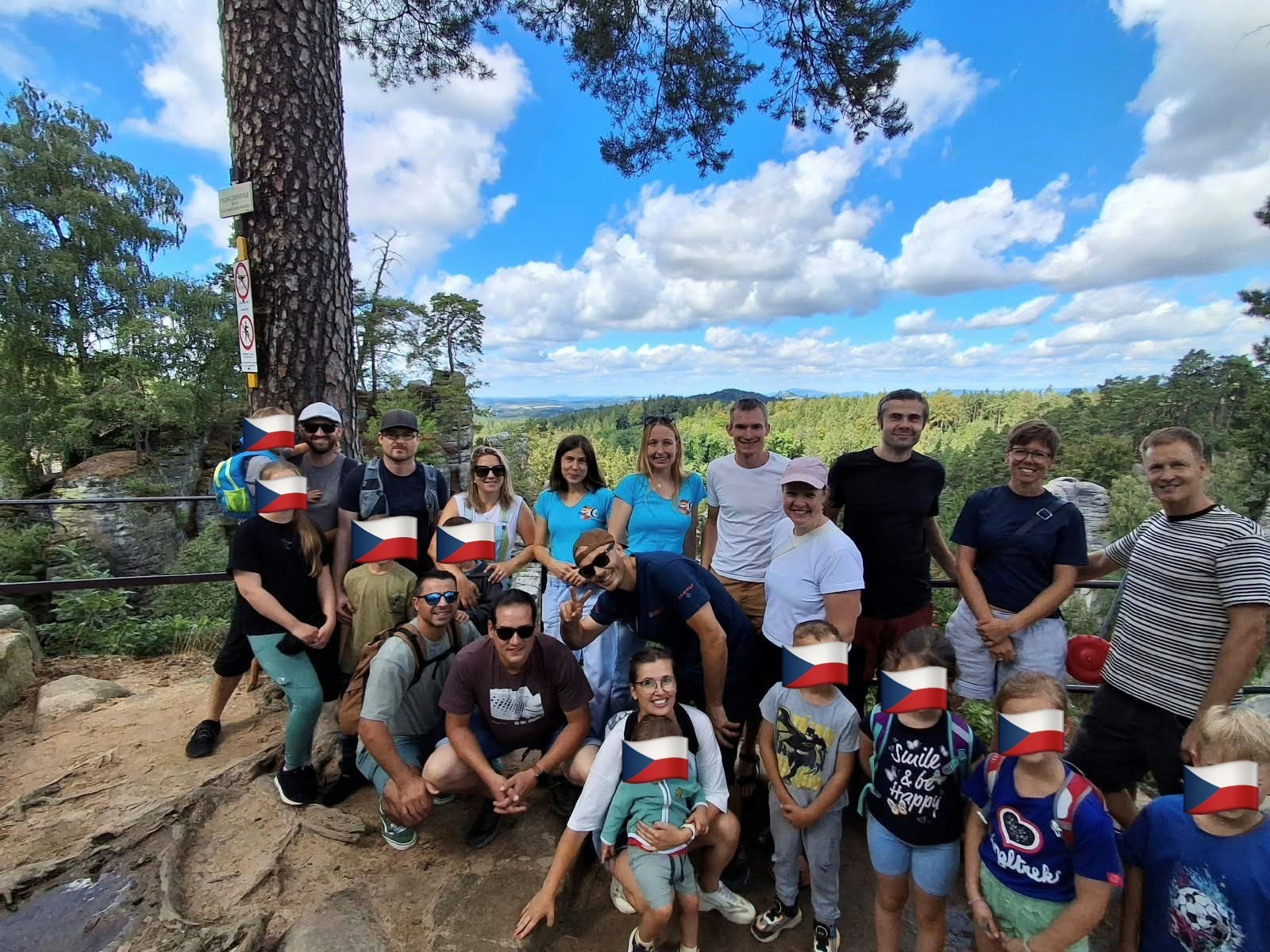Gruppenbild einer Gruppe von Männern und Frauen mit Kindern in einer Waldlandschaft. Die Kinder wurden unkenntlich gemacht.