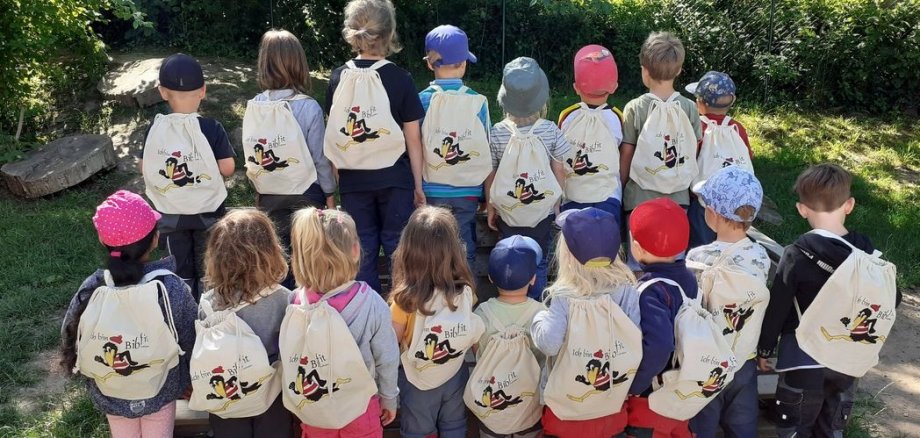 Kinder in der Rückansicht mit Rucksäcken in einem Garten