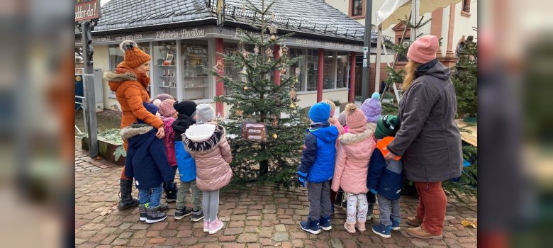 Kita-Kinder stehen um Weihnachtsbaum auf Marktplatz vor Brunnen