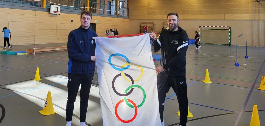 Zwei Sportcoaches halten Fahne mit olympischen Ringen hoch