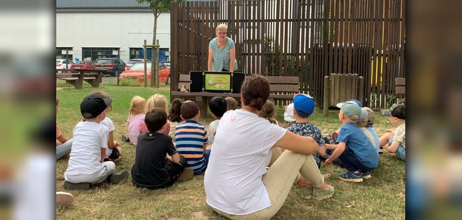 Kita-Kinder sitzen auf Wiese und hören Geschichte zu