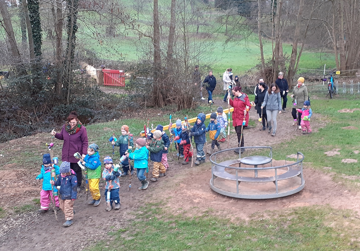 Kindergartenkinder mit Erzieherinnen auf Kindergartengelände mit bunten Stöcken