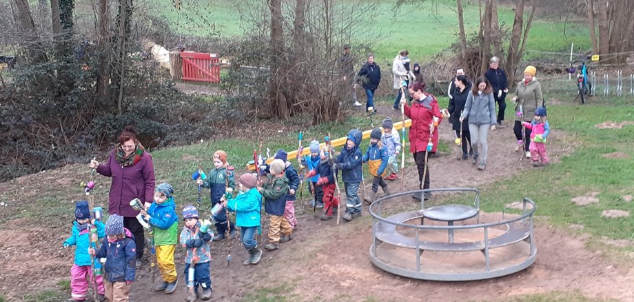 Kindergartenkinder mit Erzieherinnen auf Kindergartengelände mit bunten Stöcken