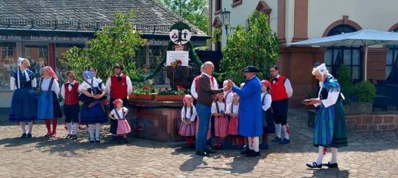 Trachtengruppe in Tracht vor geschmücktem Brunnen