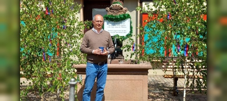 Bürgermeister mit Tonbecher in der Hand vor geschmücktem Brunnen